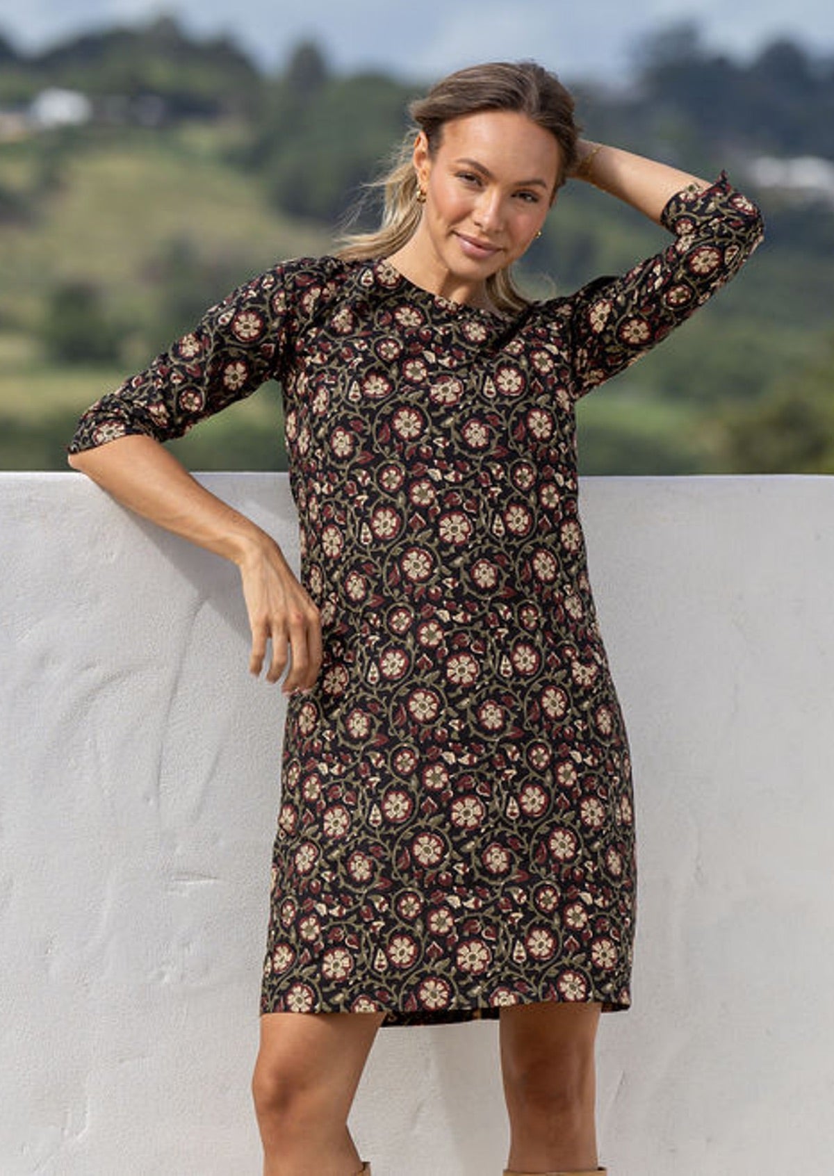 Woman wearing a deep maroon, olive and natural floral print on a black base, cotton above knee, 3/4 sleeve dress