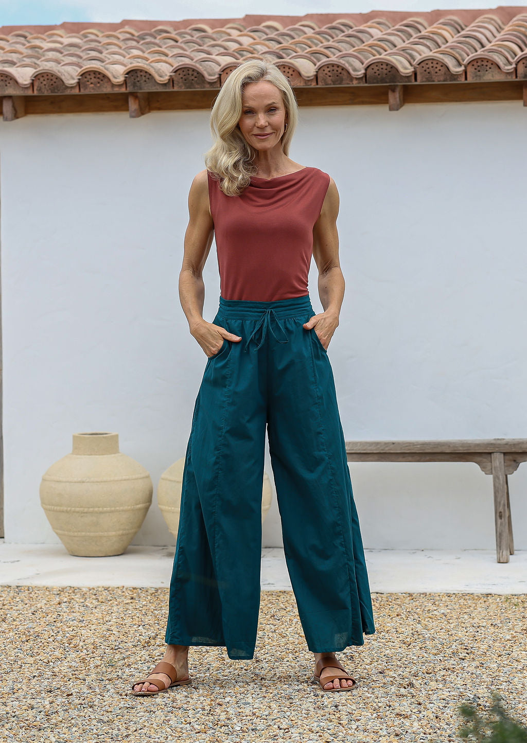Woman wearing a cowl neck top and deep teal wide-leg pants with pockets, drawstring and elasticated waist.