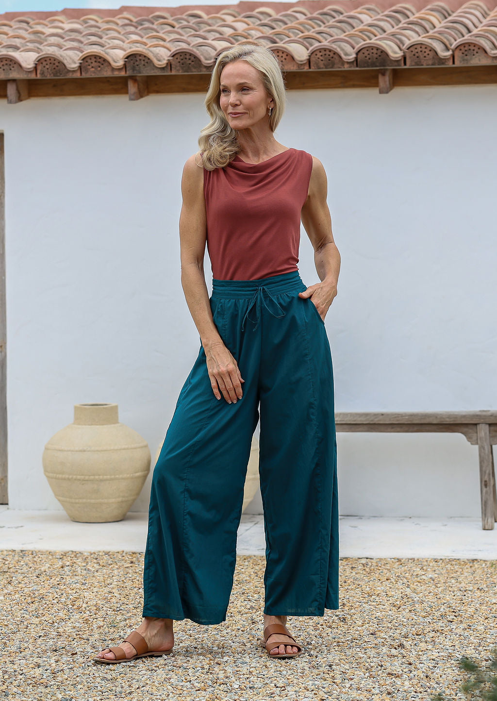 Woman poses in relaxed fit wide-leg cotton pants in deep teal with pockets, elastic waist and drawstring tie.