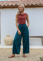 Woman poses in relaxed fit wide-leg cotton pants in deep teal with pockets, elastic waist and drawstring tie.
