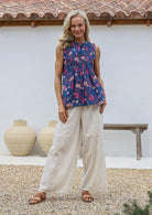 Woman wearing a sleeveless floral top and wide-leg cotton pants with elastic waist and drawstring tie, standing outdoors with a white wall and wooden bench in the background.
