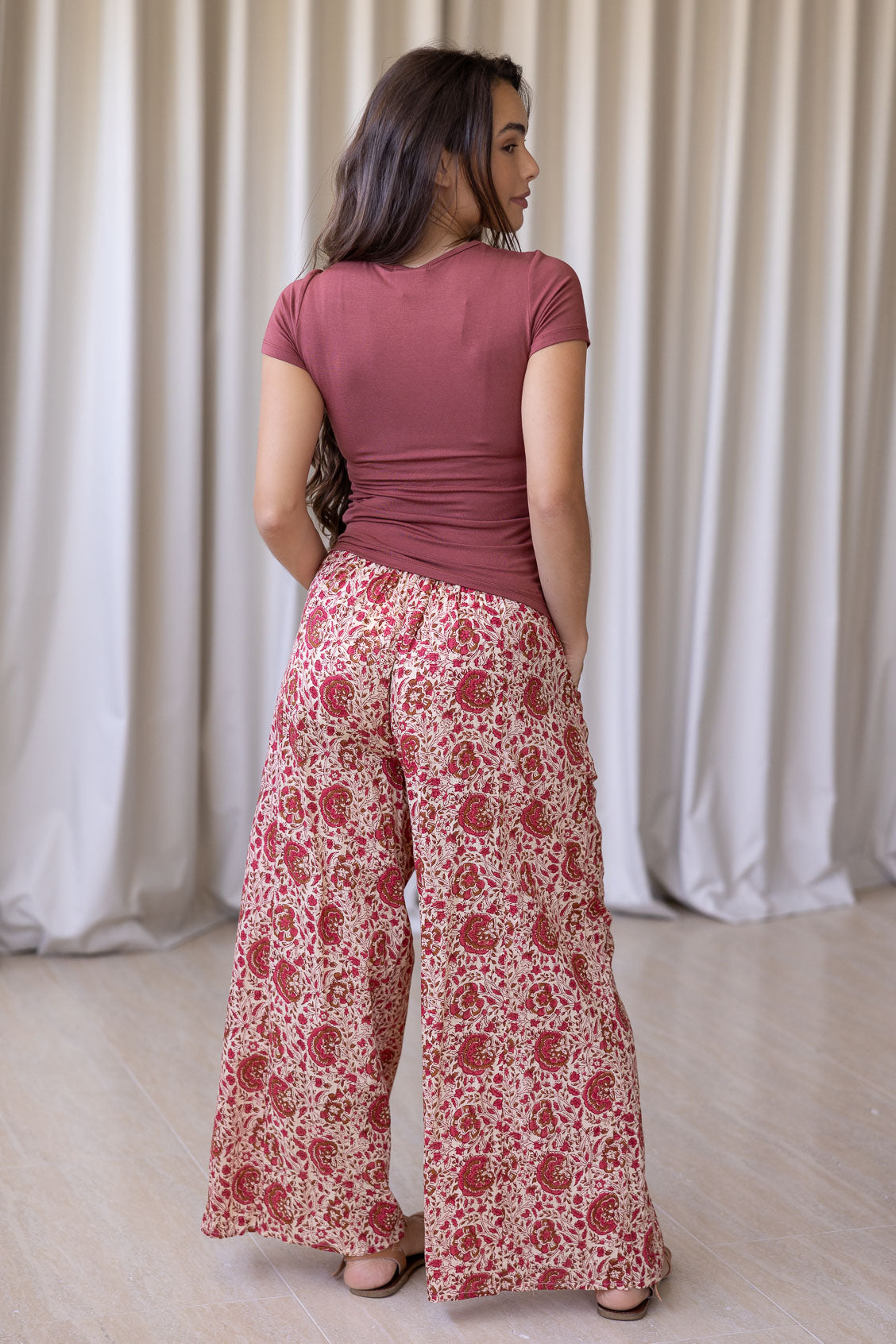 Model stands backwards wearing high waisted, relaxed fit cotton pants with drawstring and a hand in pocket. 