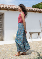 woman stands sideways wearing a wide legged rayon pants with blue based pink and white floral print.