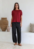 Woman wearing a maroon soft stretch rayon batwing top and black pants in a minimalistic room.