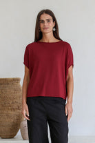Woman wearing a maroon short sleeve batwing top with a round neckline, paired with black pants