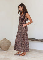 Woman wearing a Indian patterned cotton dress standing in a minimalistic room with her hands in her pockets 