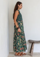 Model stands sideways wearing a 100% cotton 3 tiered maxi dress with flowy skirt, 3/4 sleeves, buttoned bodice and pockets.