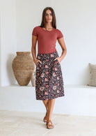 Woman posing in black based floral print skirt with side zipper and piped detailing at the waistband and pockets 