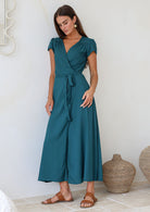 Woman leaning on a wall in a teal rayon wrap dress with gathers across front of shoulders