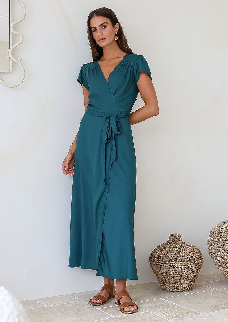 Woman wearing a teal rayon wrap long dress standing in a room with decorative vases.