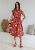 Model posing in a red floral print shirt style 100% cotton dress with cap sleeves and detachable waist tie