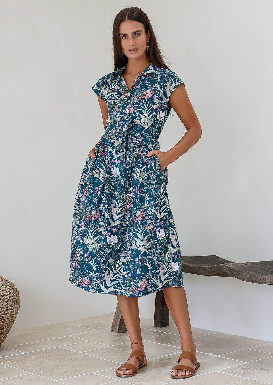 Woman wearing a shirt style cotton midi length dress with buttoned bodice, pockets, collar and cap sleeves