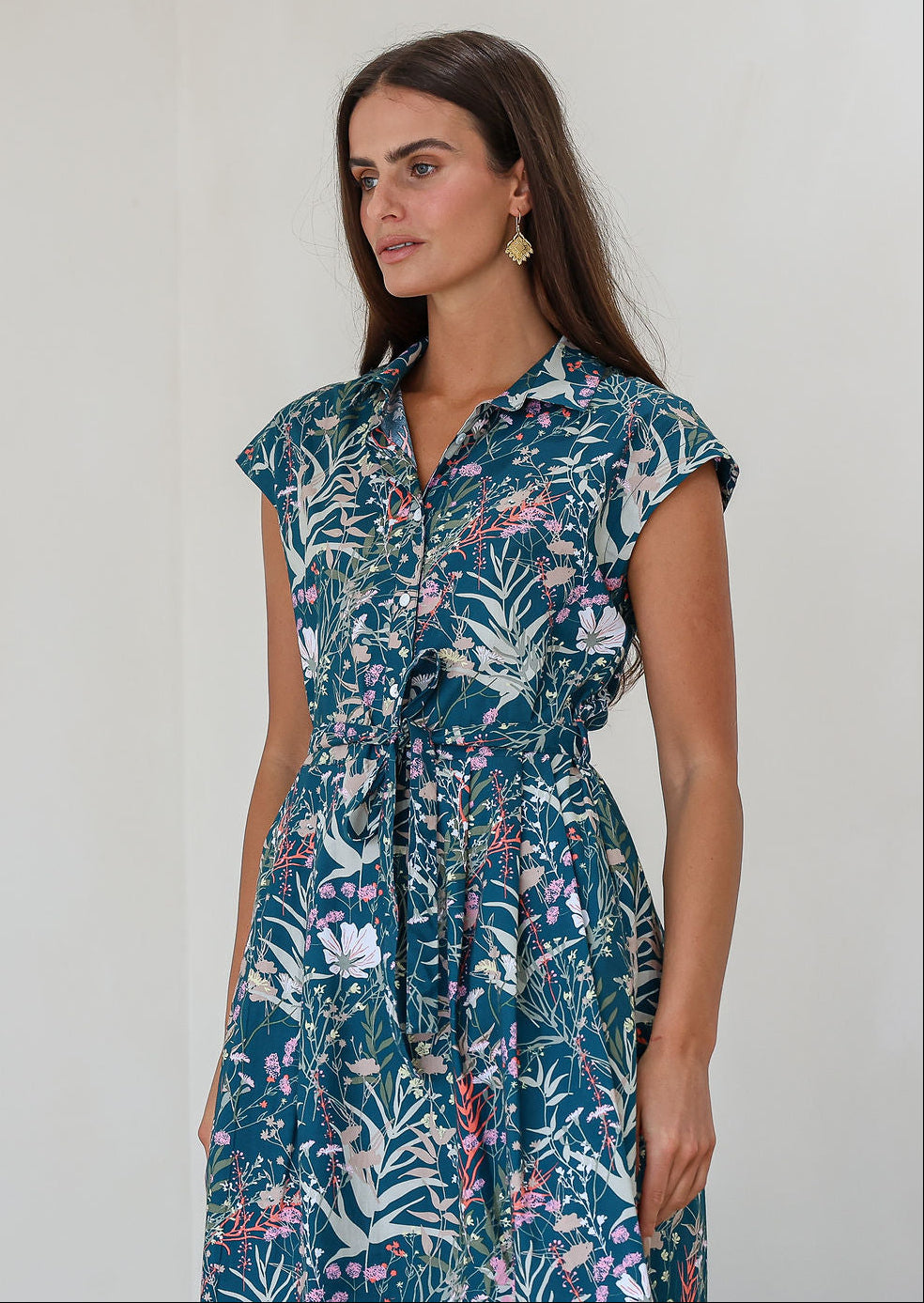Model posing in a teal based floral print shirt style 100% cotton dress with cap sleeves and detachable waist tie