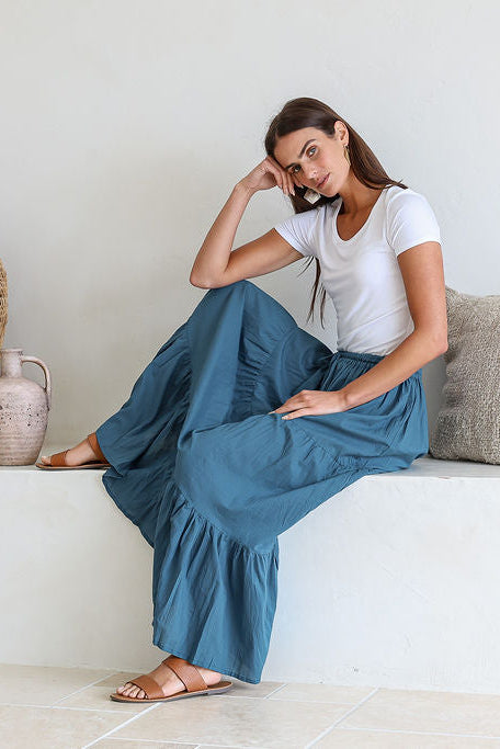 Woman sitting on a white bench wearing a 100% cotton maxi skirt in corsair blue and white plain top.