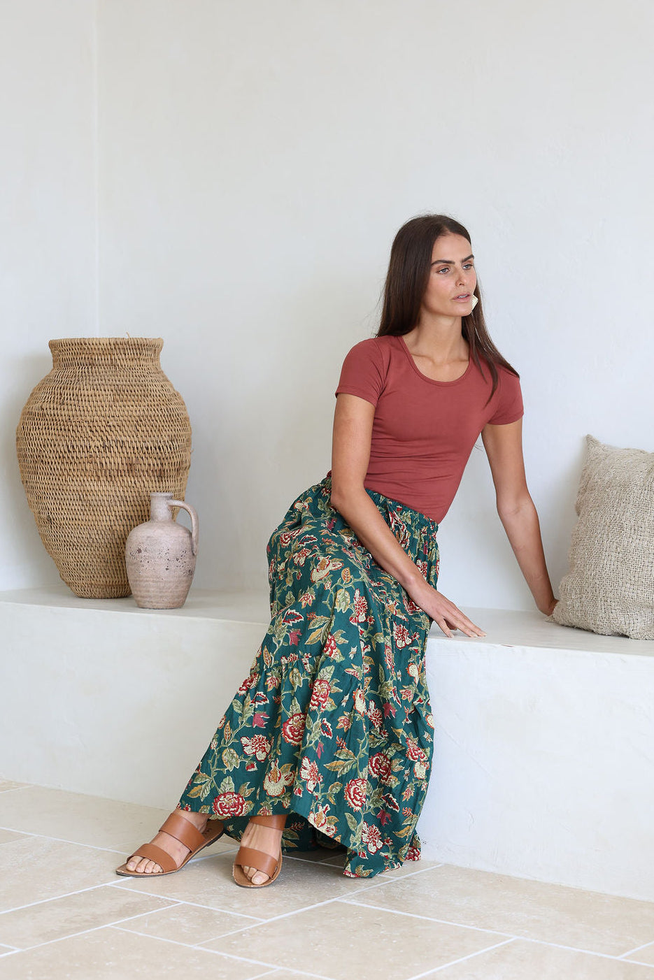 Woman sitting on a white bench wearing a green based floral print 100% cotton maxi skirt.