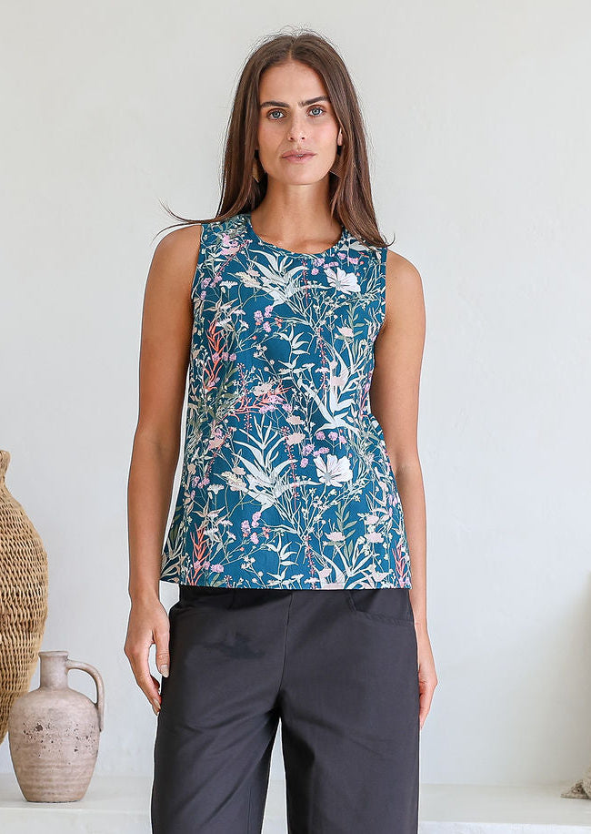 Woman wearing a sleeveless retro floral 100% cotton top with round neckline standing in a room with decorative vases.
