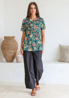 Woman wearing a relaxed fit 100% cotton top in a bottle green based floral print with short sleeves, pockets and gathers under the bust