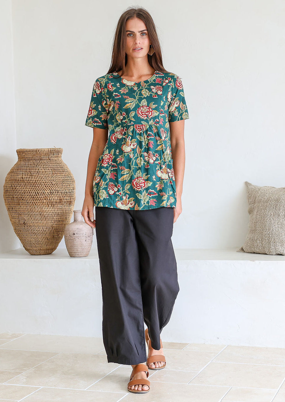 Woman wearing a relaxed fit 100% cotton top in a bottle green based floral print with short sleeves, pockets and gathers under the bust