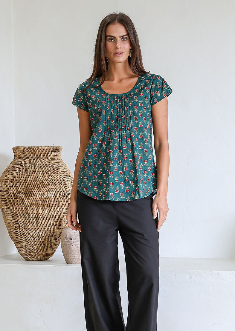 Woman wears bottle green based floral 100t% cotton cap sleeve top with pin tuck detail across the bust and a scoop neckline