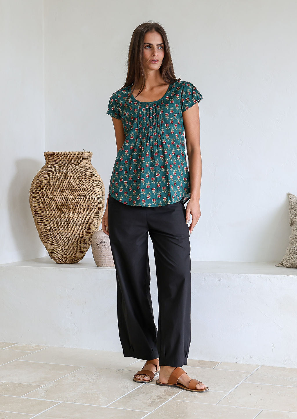 Woman wearing a bottle green based floral print short sleeve top with scoop round neckline and pleated detail across the bodice