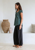 Woman standing sideways wears 100 percent cotton top with short cap sleeves and longer back hem.