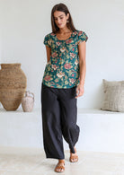 Woman wearing a bottle green based floral print short sleeve top with scoop round neckline and pleated detail across the bodice