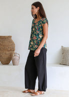 Woman standing sideways wears 100 percent cotton top with short cap sleeves and longer back hem.