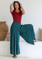 Woman with leg up on step wearing a maroon top and teal wide leg rayon pants with a ruched waistband