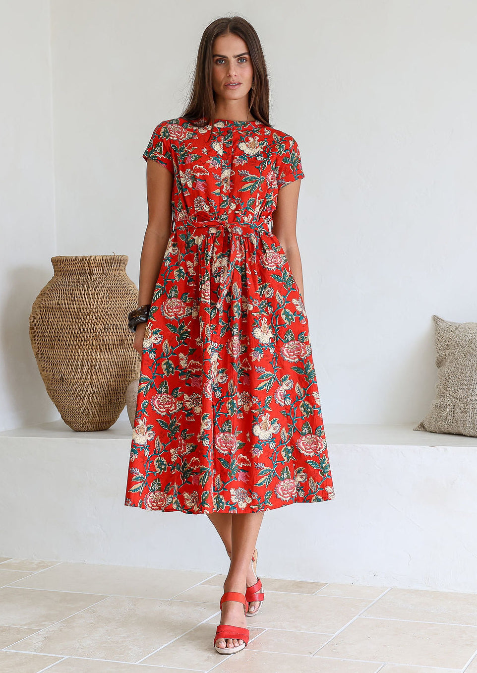 Woman wears retro style cotton button through midi length dress with high round neckline, short sleeves and a removable waist tie.