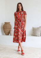 Woman wears 100% cotton button through midi length dress with short sleeves and pockets in floral print on a red base.