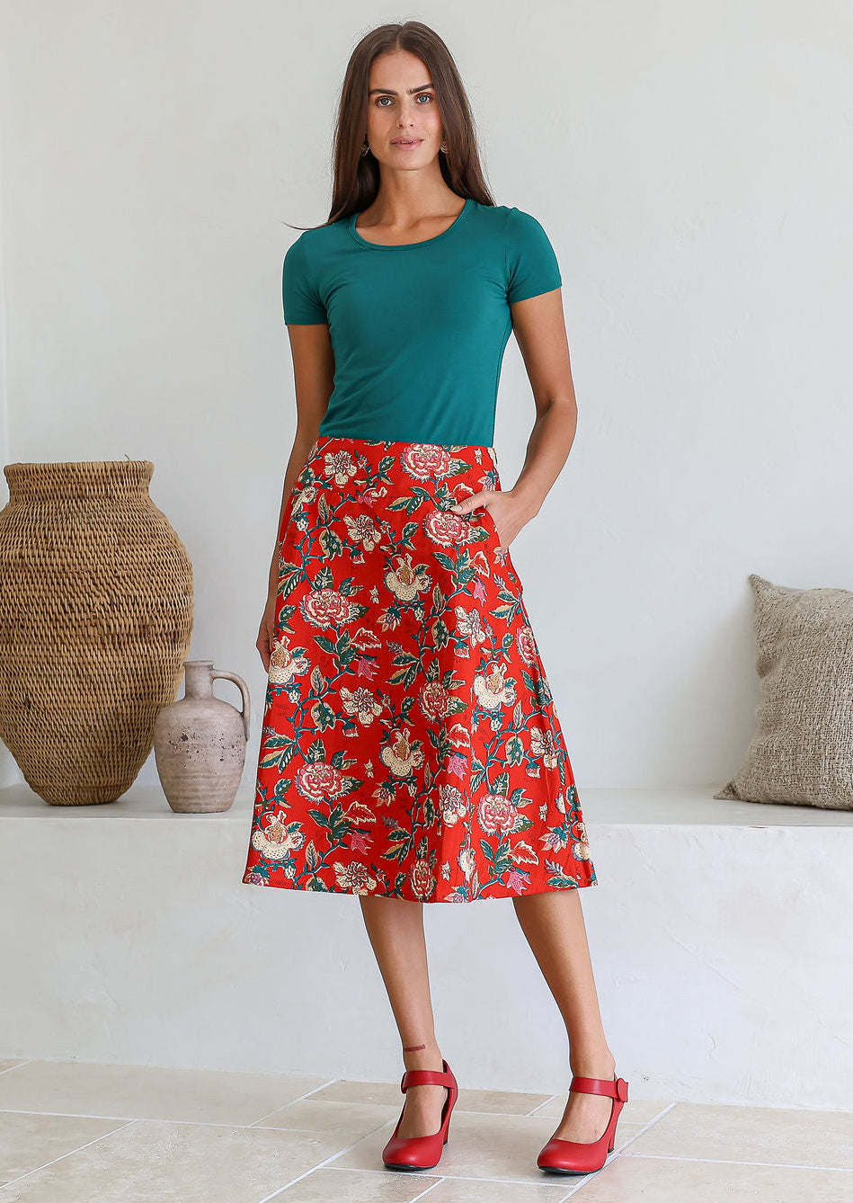 Woman wearing a basic green top and red floral a-line cotton skirt with side zipper and one hand in pocket.