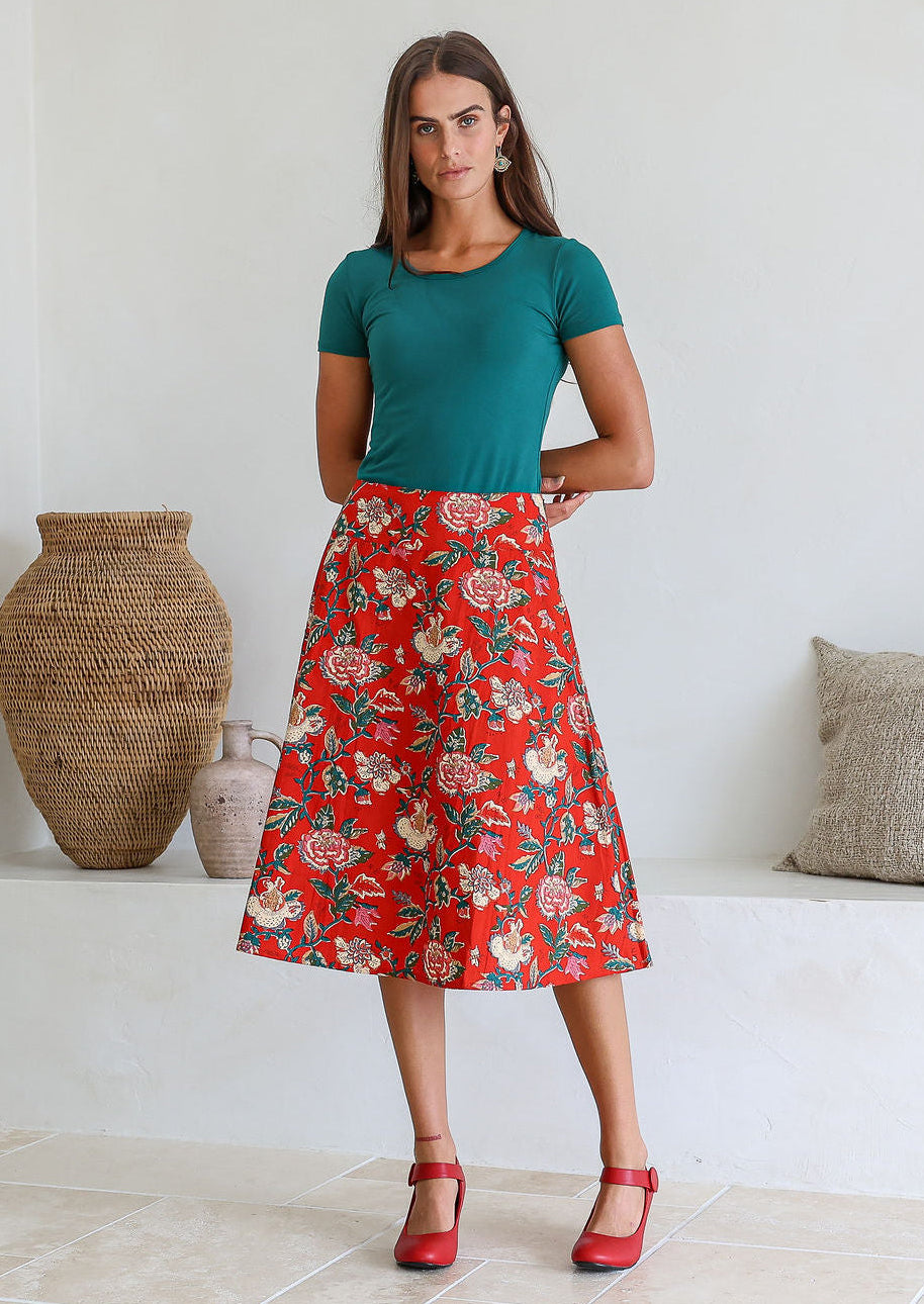 Woman wearing a green top and red floral cotton skirt in a room with decorative vases.