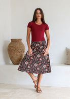 Woman wearing a basic maroon top and black floral a-line cotton skirt with side zipper and pockets.