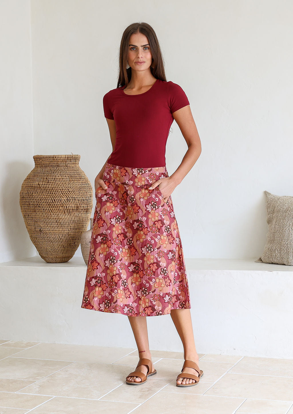 Woman wearing a basic maroon top and warm toned floral a-line cotton skirt with side zipper and both hands in pocket.