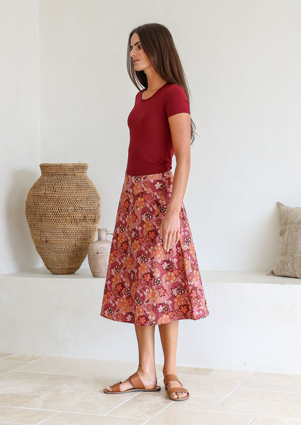 woman stands sideways wearing a knee length floral cotton skirt with a-line shape, pockets and side zipper.