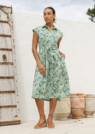 Woman wearing a shirt style cotton midi length dress with buttoned bodice, pockets, collar and cap sleeves