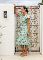 Woman in a cotton floral dress standing against a decorative wall.