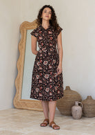 Woman wearing a shirt style cotton midi length dress with buttoned bodice, pockets, collar and cap sleeves