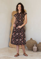 Model posing in a black floral print shirt style 100% cotton dress with cap sleeves and detachable waist tie