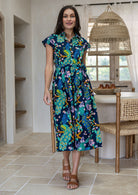 A woman modelling a cap-sleeve cotton midi dress with collar and buttoned bodice, in a vibrant multicolour floral and peacock print