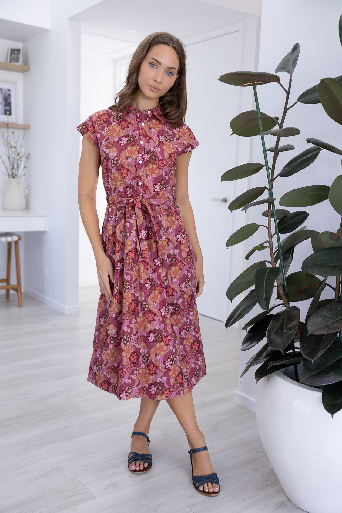Woman wearing a midi length Japanese style floral print cotton dress with buttoned bodice, standing in a room.