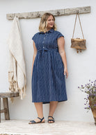 Woman wearing a midi length navy based white stripes print cotton dress with buttoned bodice 
