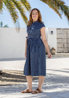 Model posing in a navy based white striped print shirt style 100% cotton dress with cap sleeves and detachable waist tie