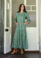 Woman poses in sage green based floral cotton maxi dress with buttoned bodice, 3/4 sleeves and flowy three tiered maxi skirt