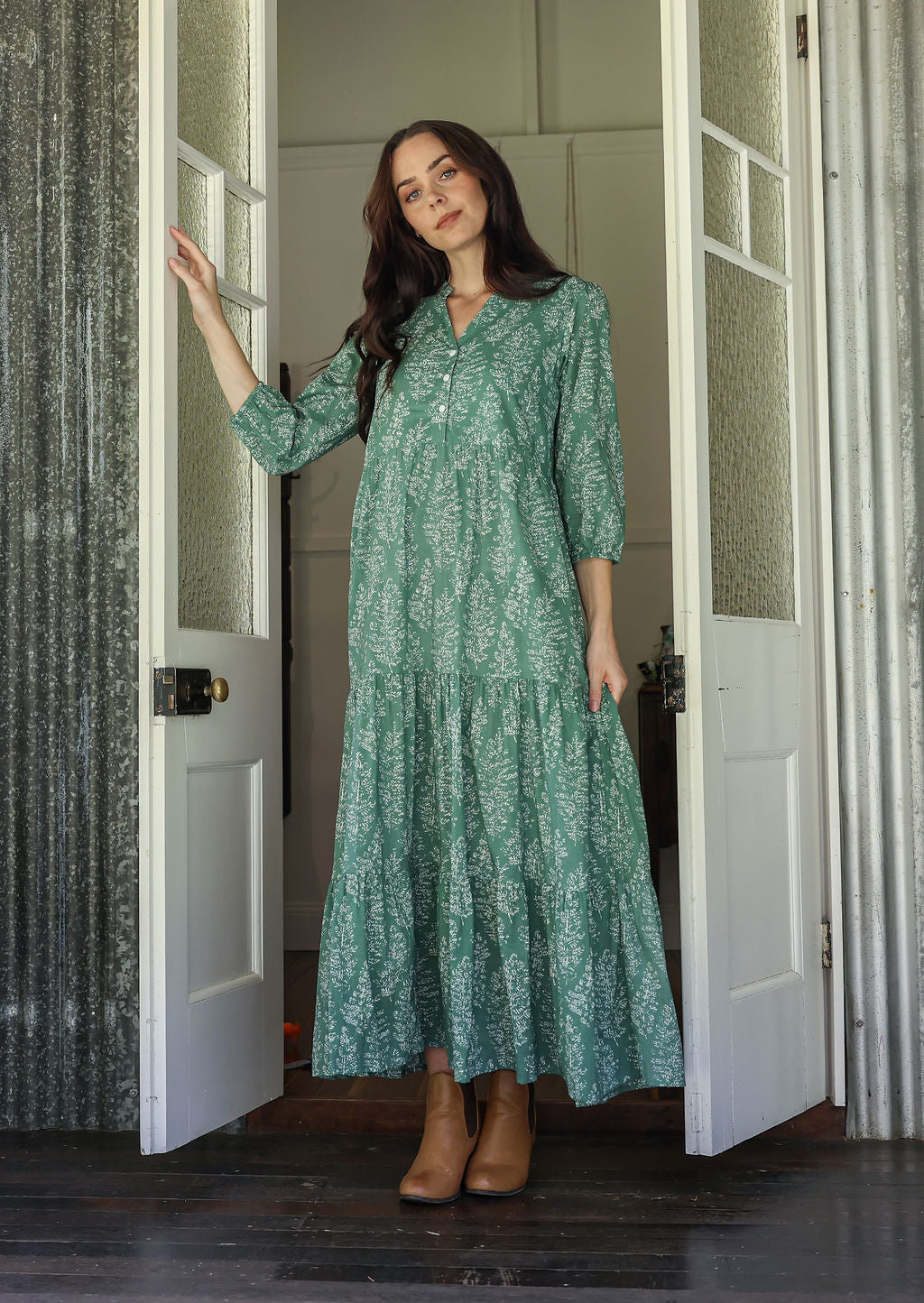 Woman standing in sage green based 100% cotton flowy tiered maxi dress with 3/4 sleeves, buttoned bodice and pockets 