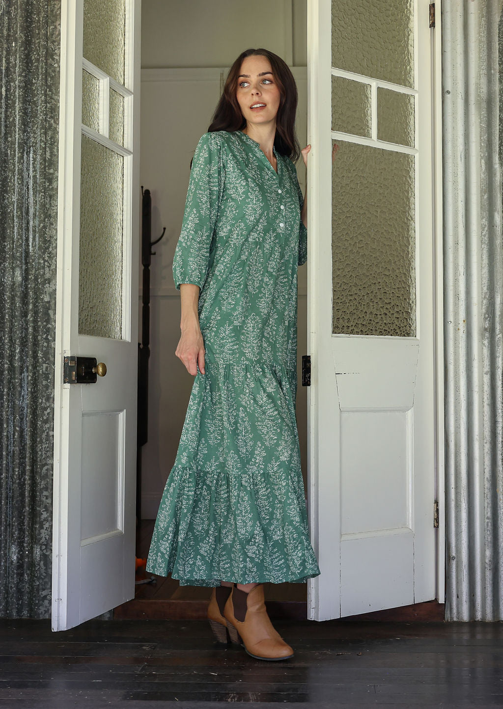 Woman stands side ways wearing a 100% cotton tiered maxi dress in cream based floral print with 3/4 sleeves