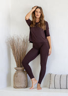 Woman leaning against a wall wearing dark brown stretch rayon jersey top and leggings