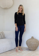Woman wearing a 100% rayon jersey soft stretch leggings in navy blue standing in a minimalistic room. 