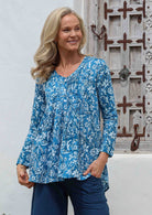 Woman wearing a blue floral relaxed fit a-line cotton blouse with V neckline, long sleeves, button through front and small pleats at front and back.