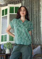 Woman wearing a sage green based relaxed fit, shirt style floral cotton top with plain pants.